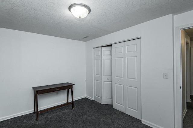 unfurnished bedroom featuring dark colored carpet, a closet, baseboards, and a textured ceiling