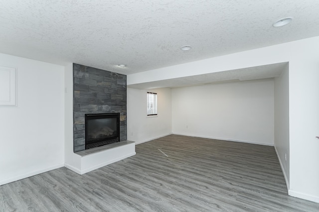 unfurnished living room with a textured ceiling, wood finished floors, baseboards, and a large fireplace