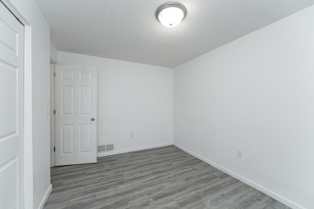 empty room with baseboards, wood finished floors, visible vents, and a textured ceiling