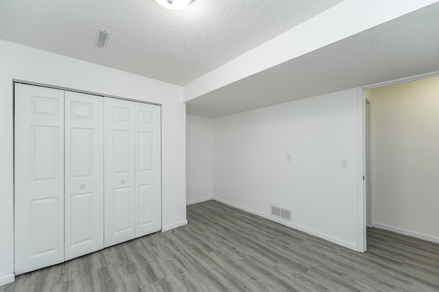 unfurnished bedroom with visible vents, a textured ceiling, baseboards, and wood finished floors