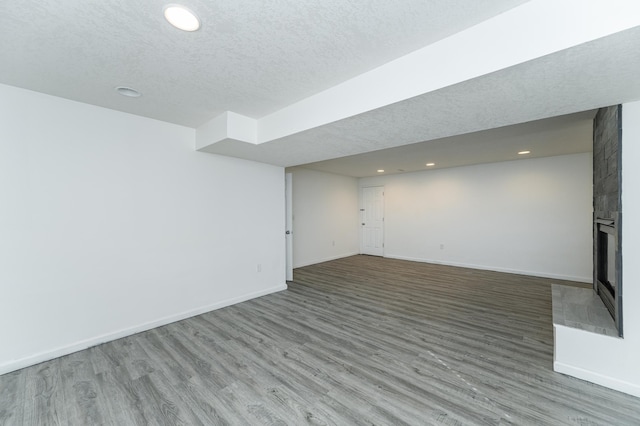 finished basement with wood finished floors, baseboards, a fireplace, recessed lighting, and a textured ceiling