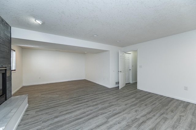 unfurnished living room featuring a fireplace, a textured ceiling, baseboards, and wood finished floors