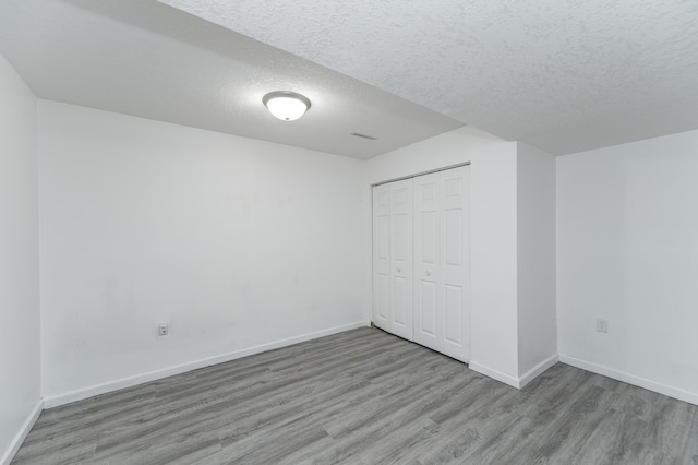 unfurnished bedroom featuring a closet, a textured ceiling, baseboards, and wood finished floors