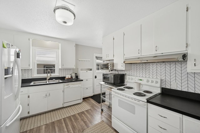 kitchen with under cabinet range hood, white appliances, a sink, white cabinetry, and dark countertops