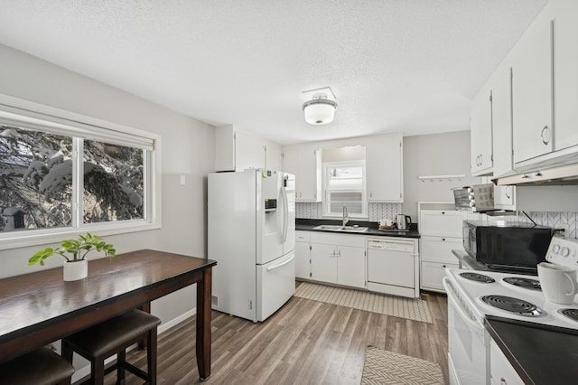 kitchen with light wood finished floors, dark countertops, decorative backsplash, a sink, and white appliances