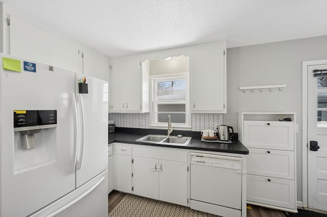 kitchen featuring dark countertops, backsplash, white cabinets, a sink, and white appliances