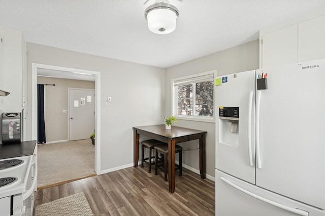 kitchen with white appliances, baseboards, white cabinets, wood finished floors, and a textured ceiling