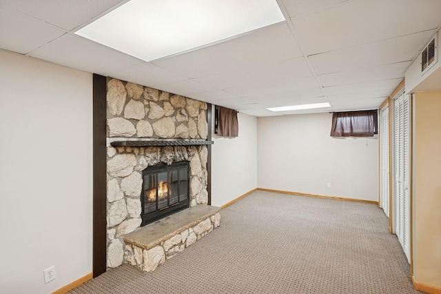 finished basement with a paneled ceiling, light colored carpet, a stone fireplace, and baseboards