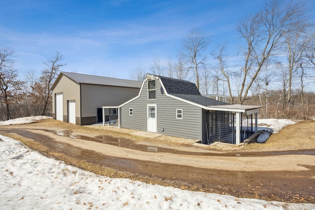 view of side of property with an outbuilding, a garage, dirt driveway, and a shingled roof