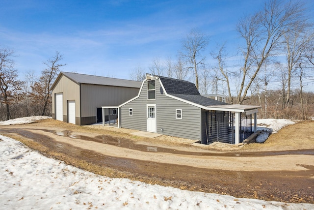 view of home's exterior with a detached garage, a gambrel roof, an outdoor structure, and a shingled roof