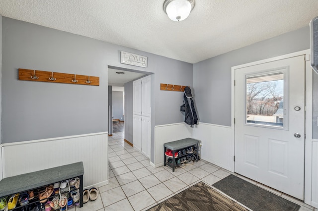 entrance foyer with light tile patterned flooring, a wainscoted wall, and a textured ceiling