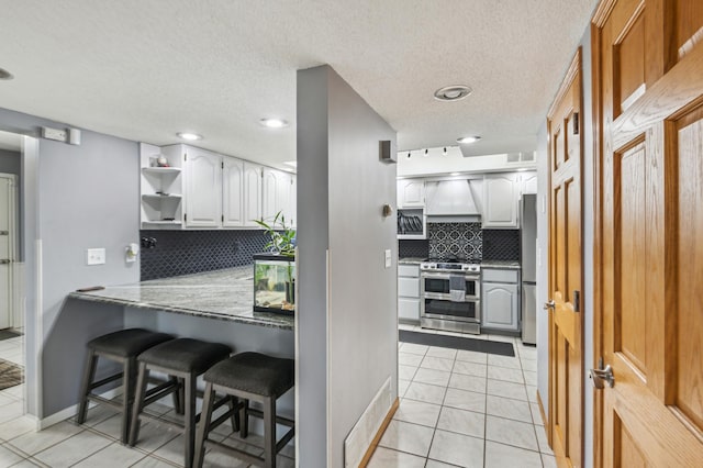 kitchen featuring open shelves, a kitchen breakfast bar, appliances with stainless steel finishes, light tile patterned flooring, and white cabinets