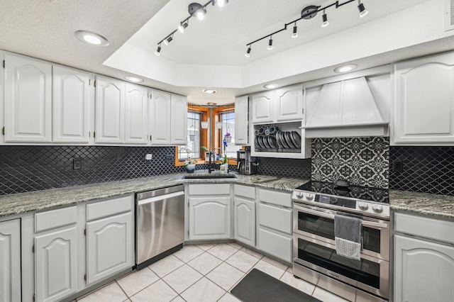 kitchen with custom range hood, light tile patterned floors, decorative backsplash, stainless steel appliances, and a sink