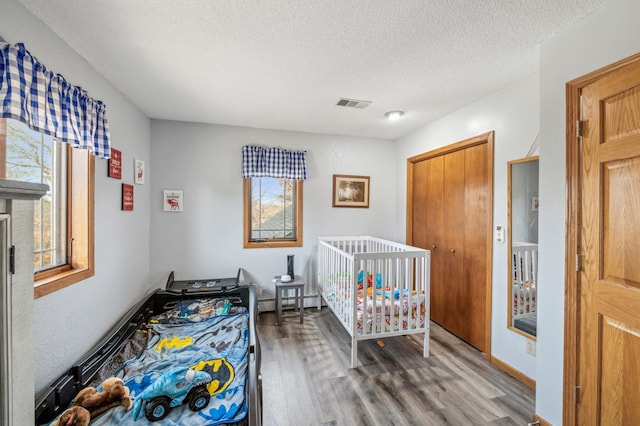 bedroom with a baseboard radiator, wood finished floors, visible vents, and a textured ceiling