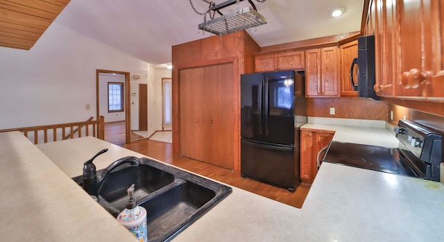 kitchen with brown cabinets, a sink, black appliances, vaulted ceiling, and light wood-type flooring