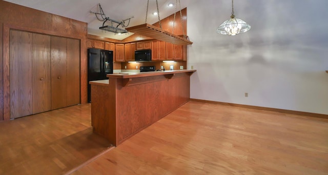 kitchen featuring brown cabinets, black appliances, a breakfast bar, light wood-style floors, and a peninsula