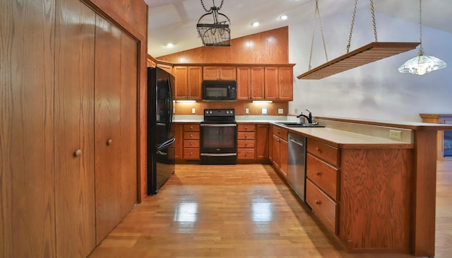 kitchen with brown cabinetry, a sink, black appliances, vaulted ceiling, and light wood-type flooring