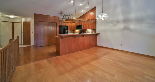 kitchen featuring light wood-type flooring, brown cabinets, black appliances, decorative light fixtures, and a peninsula