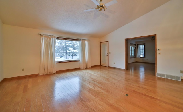 spare room featuring visible vents, a healthy amount of sunlight, light wood-style floors, and vaulted ceiling