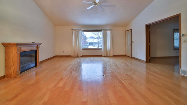 unfurnished living room featuring visible vents, baseboards, lofted ceiling, a glass covered fireplace, and light wood-type flooring