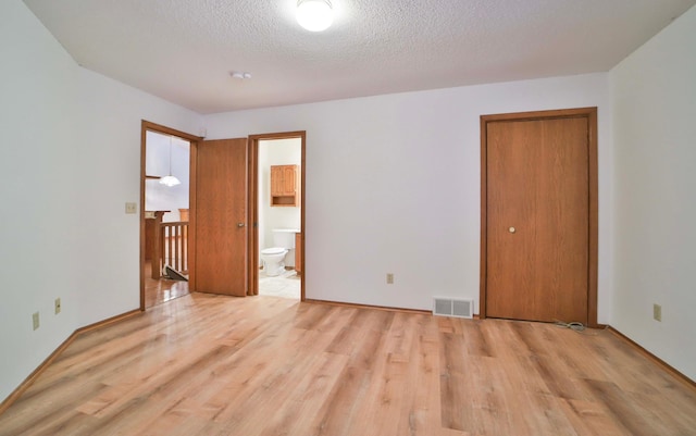 unfurnished bedroom featuring visible vents, a textured ceiling, ensuite bath, wood finished floors, and a closet