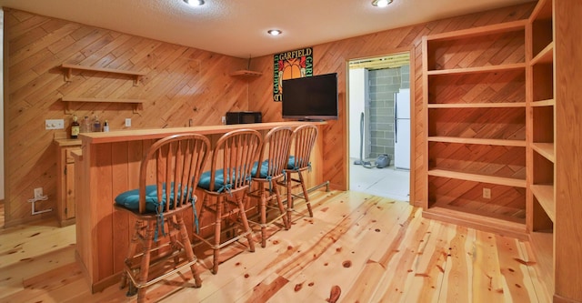 bar with a bar, wooden walls, wood finished floors, and freestanding refrigerator