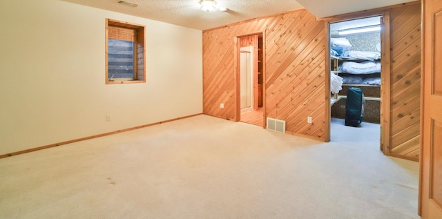 unfurnished bedroom with visible vents, a textured ceiling, carpet, wood walls, and baseboards