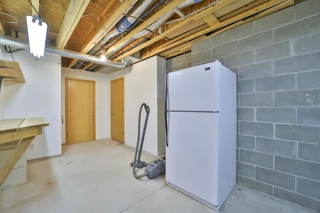 unfinished below grade area featuring concrete block wall and freestanding refrigerator