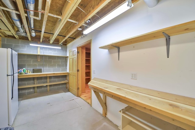 unfinished basement featuring concrete block wall and freestanding refrigerator