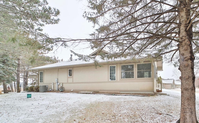 snow covered house featuring stucco siding and central AC unit