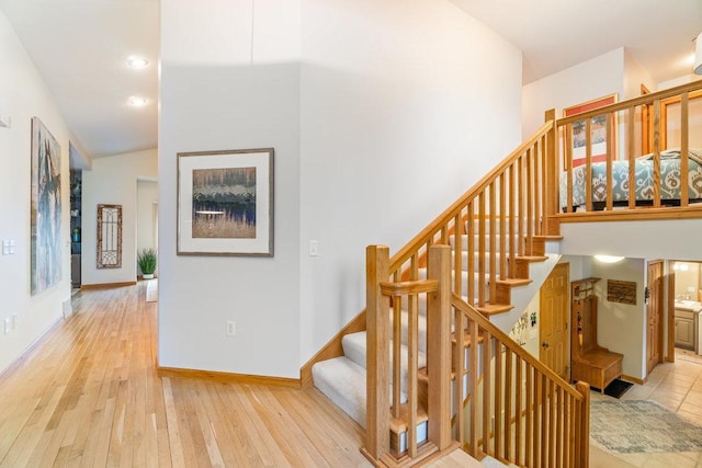 staircase with recessed lighting, a high ceiling, baseboards, and hardwood / wood-style flooring