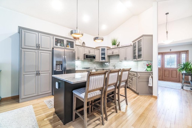 kitchen featuring a center island, gray cabinets, light stone counters, light wood-style flooring, and stainless steel appliances
