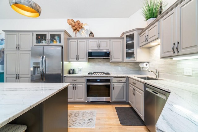 kitchen with tasteful backsplash, gray cabinetry, light stone counters, a sink, and stainless steel appliances