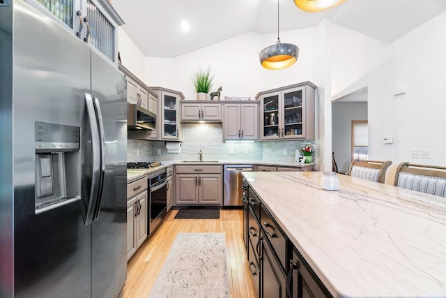 kitchen with glass insert cabinets, light wood-style floors, gray cabinets, backsplash, and stainless steel appliances