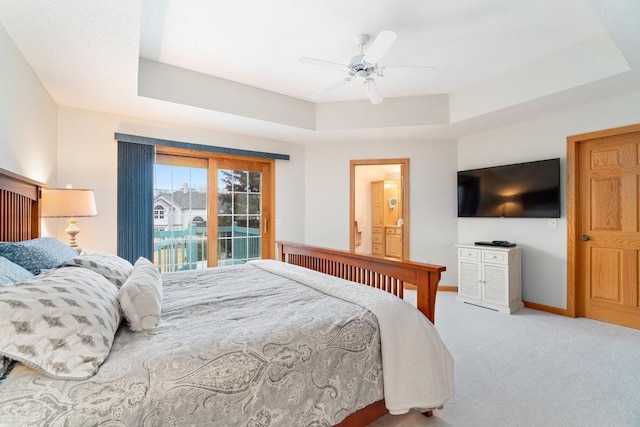 carpeted bedroom with a raised ceiling, access to exterior, a ceiling fan, baseboards, and ensuite bathroom