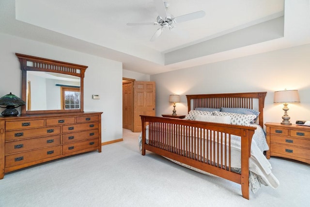 bedroom with a raised ceiling, baseboards, a ceiling fan, and light colored carpet