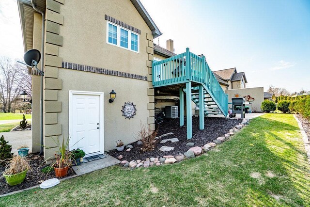 back of property with a deck, stucco siding, stairs, central air condition unit, and a yard