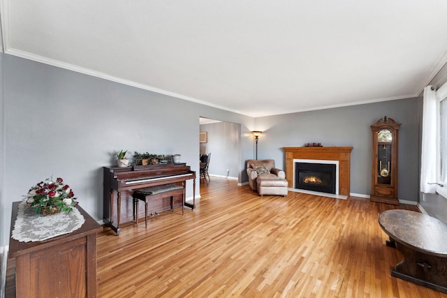 living area with a glass covered fireplace, baseboards, crown molding, and light wood finished floors