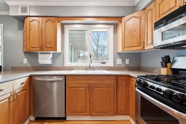 kitchen with stainless steel appliances, a sink, light countertops, and crown molding