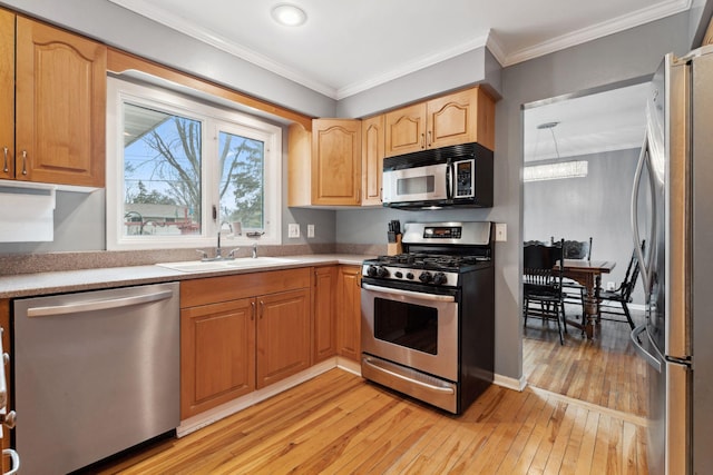 kitchen featuring light wood finished floors, ornamental molding, stainless steel appliances, light countertops, and a sink