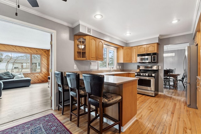 kitchen with glass insert cabinets, a peninsula, stainless steel appliances, light wood-type flooring, and a sink