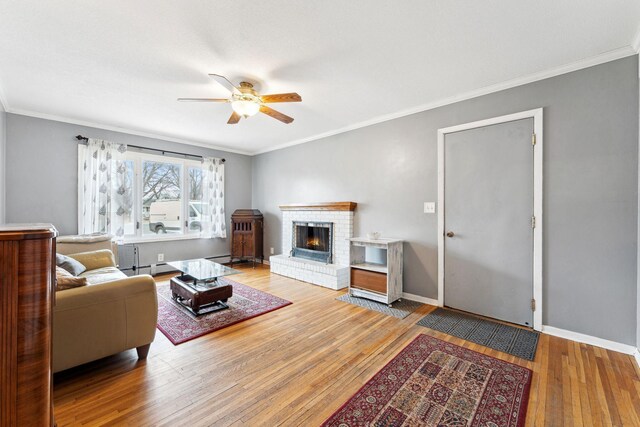 living room featuring ornamental molding, a brick fireplace, baseboards, and hardwood / wood-style flooring