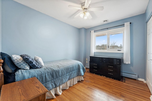 bedroom featuring light wood-type flooring, a baseboard radiator, visible vents, and baseboards