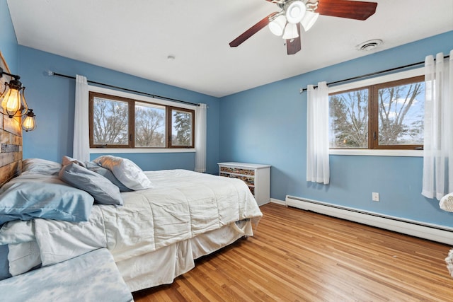 bedroom featuring a baseboard radiator, wood finished floors, visible vents, baseboards, and a ceiling fan