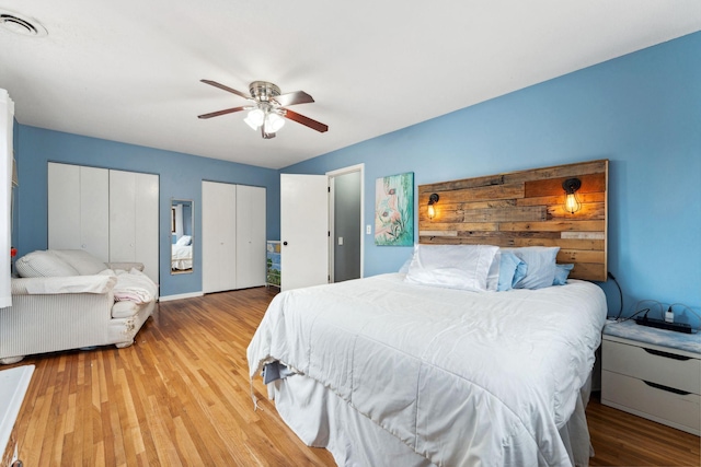 bedroom featuring ceiling fan, wood finished floors, visible vents, and multiple closets