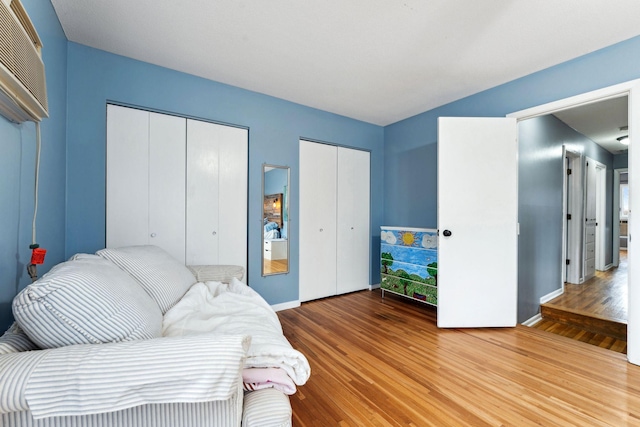 bedroom with light wood-style floors, baseboards, and two closets