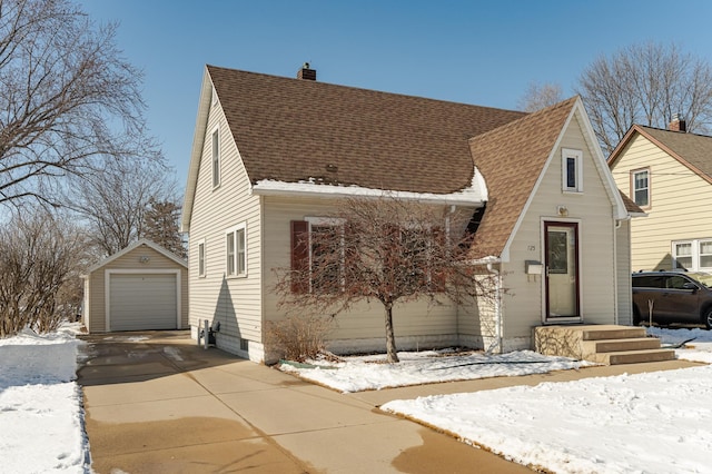 view of front of home with an outbuilding, a garage, driveway, roof with shingles, and a chimney