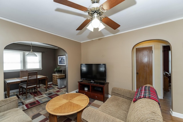 living room featuring baseboards, arched walkways, a ceiling fan, ornamental molding, and wood finished floors