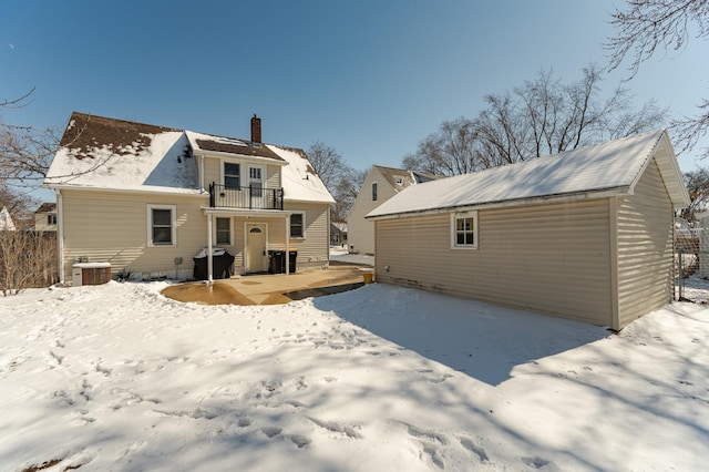 snow covered rear of property with a chimney, an outdoor structure, a balcony, and central air condition unit