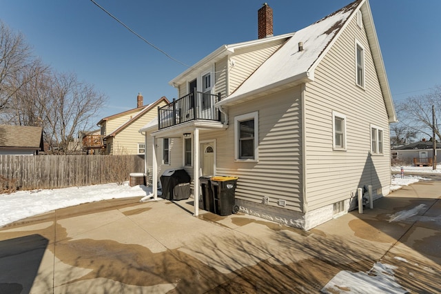 snow covered house featuring a chimney, fence, and a balcony